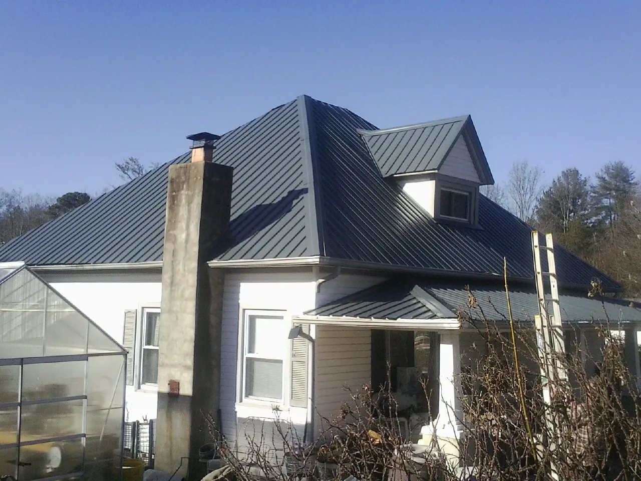 Dark blue standing seam metal roof on a white farmhouse with dormer — Slate & Tile Roof Repair by Roofing Brothers in Gwynn Oak