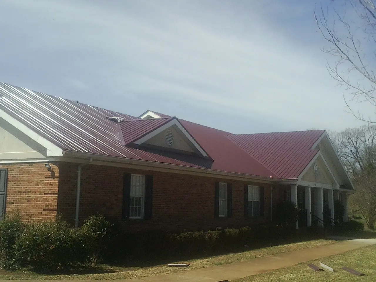 Red metal roof with gabled entries on a long brick building, from a Hail Damage Roof Repair job in Gwynn Oak