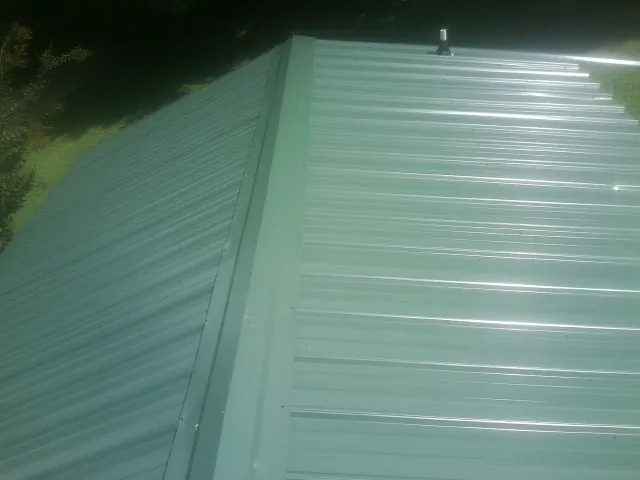 New green metal panels meeting at the ridge of a roof — Flat Roof Repair work by our crew in Gwynn Oak