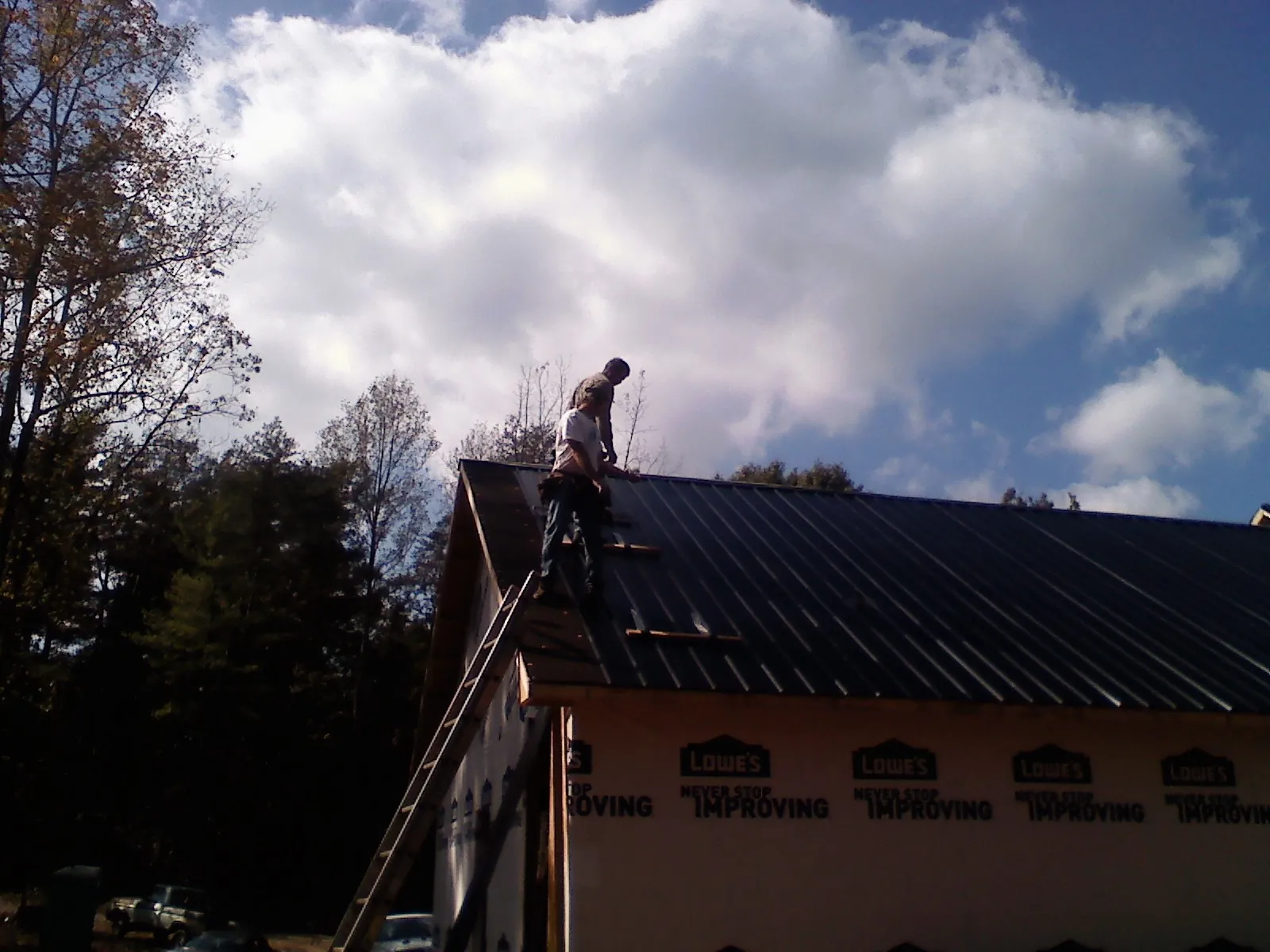 Roofer fastening dark metal panels high against a cloudy sky, from a Roof Inspection job in Gwynn Oak