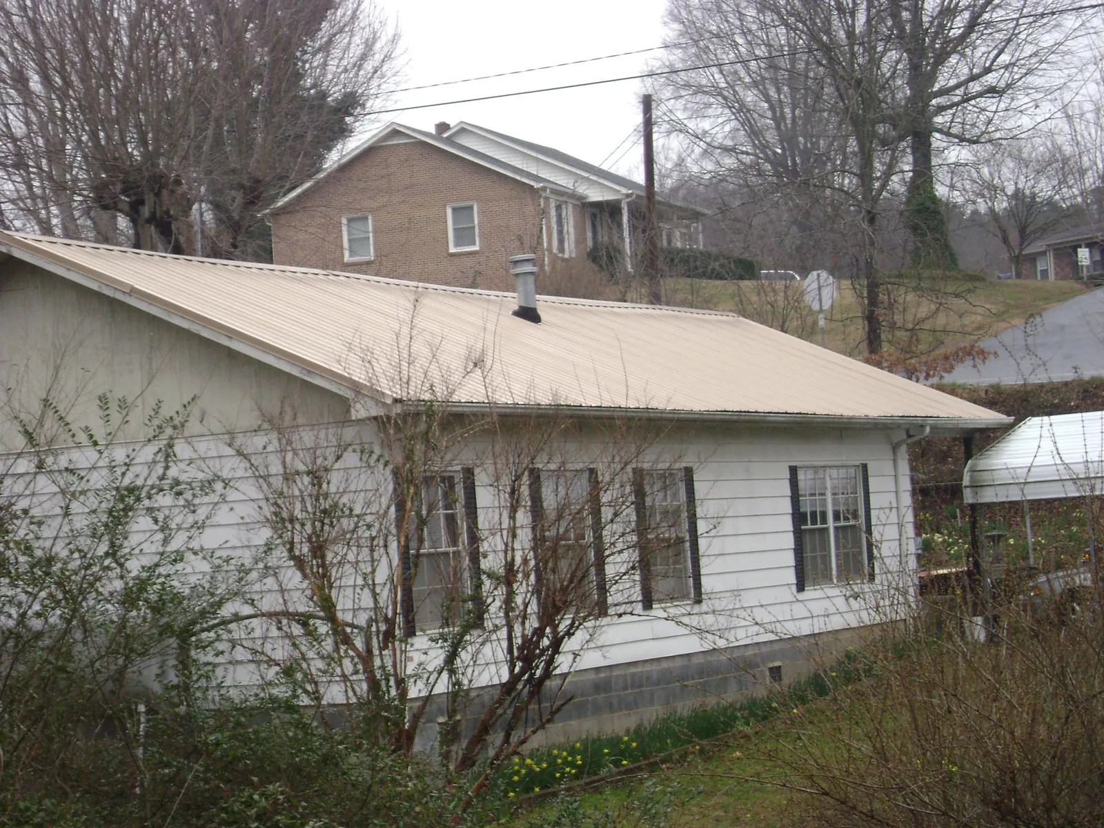 Tan metal roof on a white sided house set into a hillside — Commercial Roofing by Roofing Brothers in Gwynn Oak