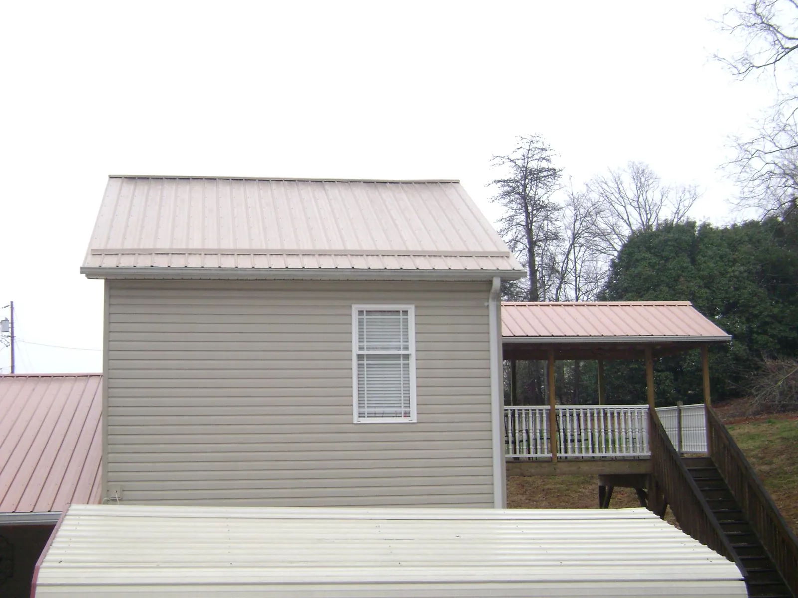 Tan metal roofs on a two story addition and attached porch, from a Roof Replacement job in Gwynn Oak